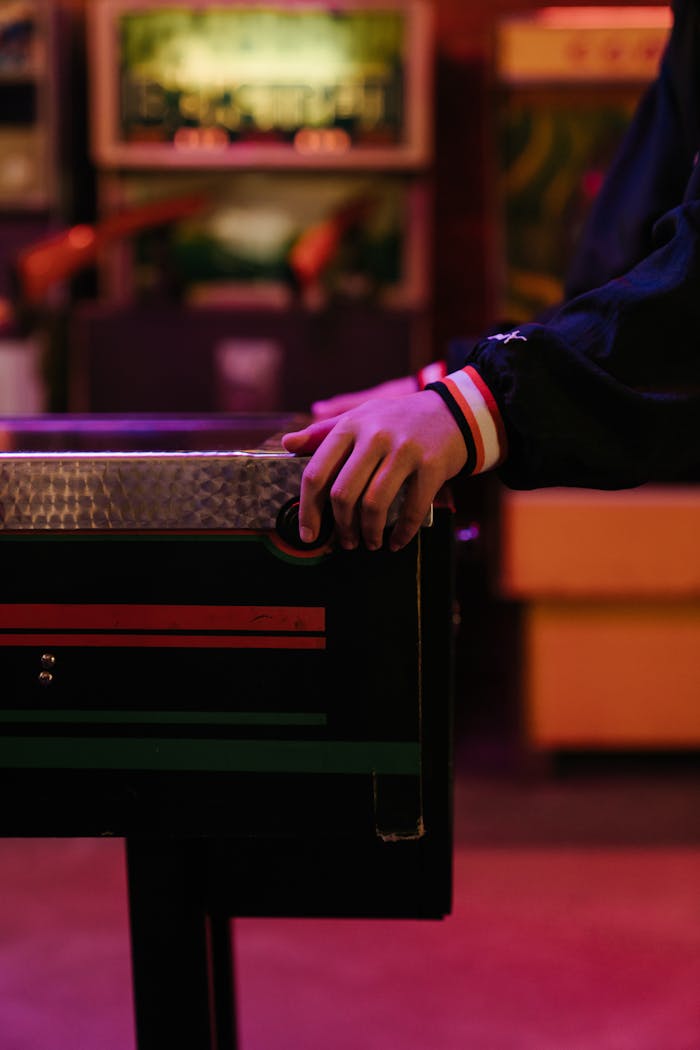 A teenager's hand on a vintage pinball machine in a vibrant arcade setting.